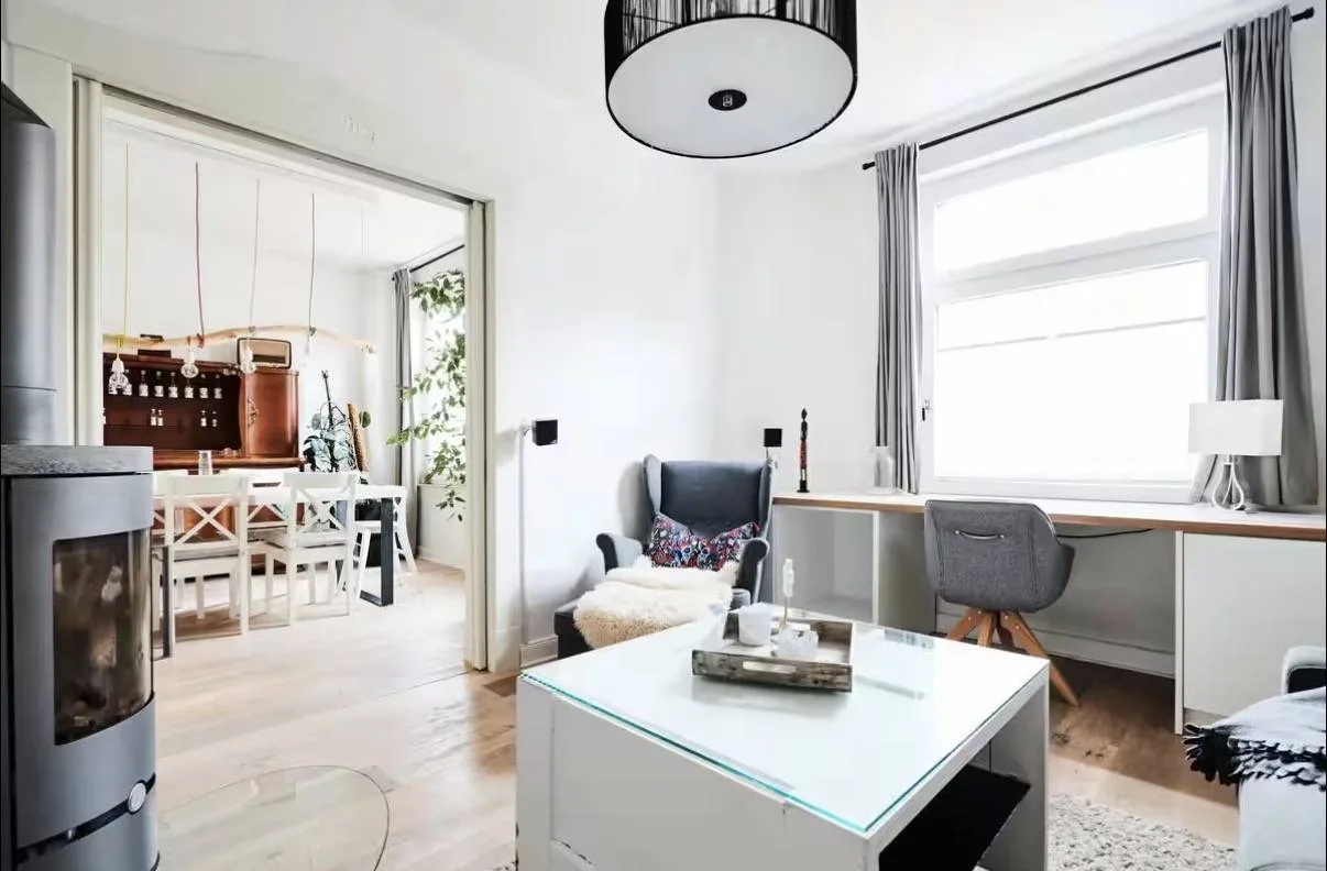 Wohnzimmer der Musterwohnung in Oldenburg mit Kaminofen, Schreibtisch unter dem Fenster und offener Schiebetür ins Esszimmer