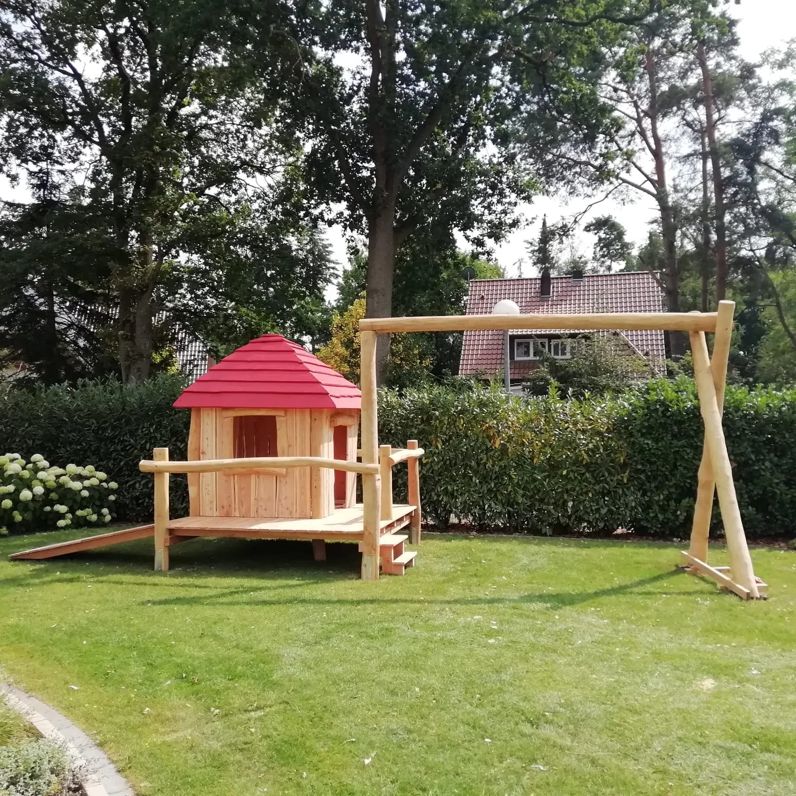 Spielhaus aus Holz mit rotem Dach im Garten